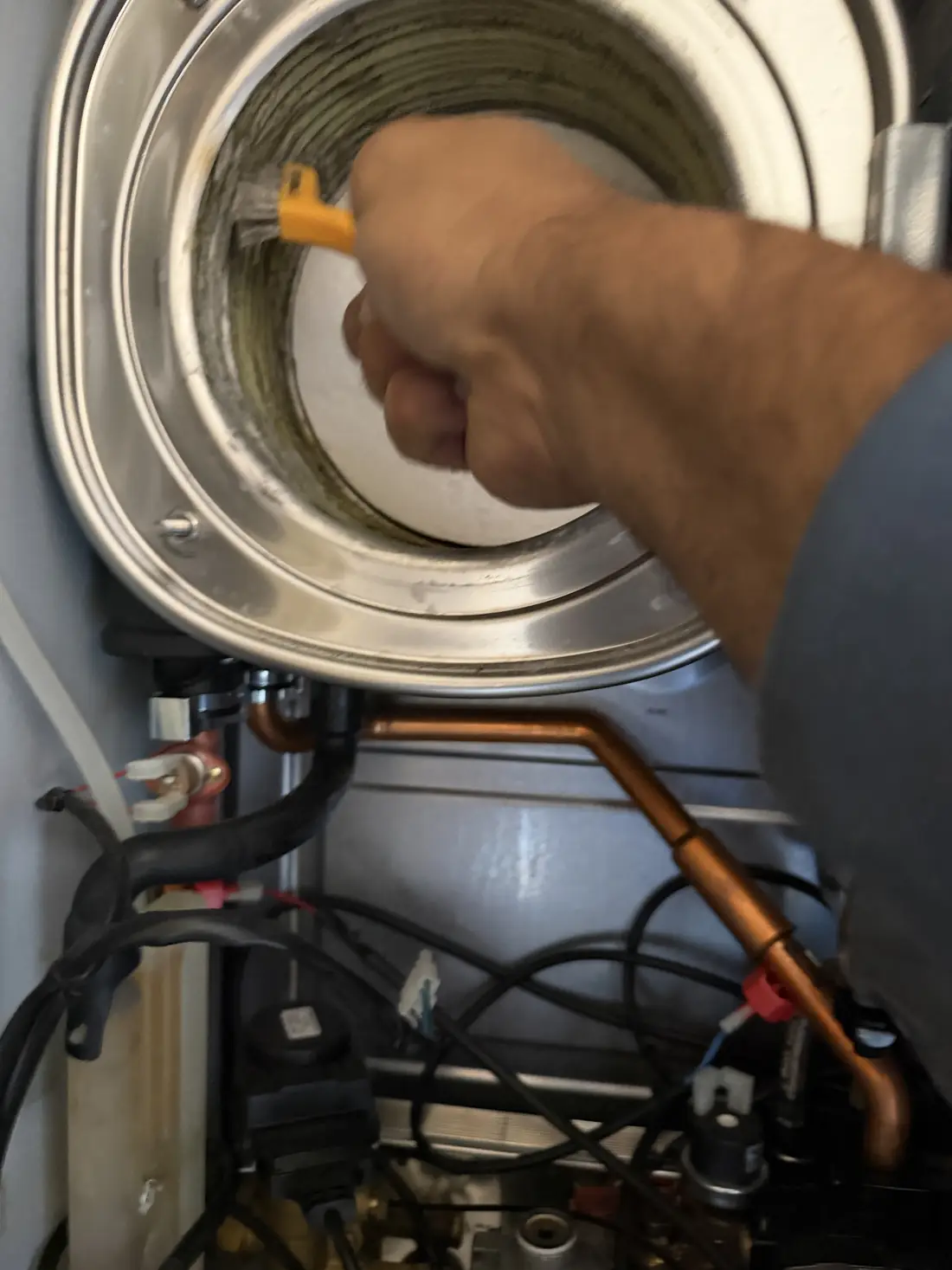 Engineer brushing the inside of the Baxi 800 heat exchanger with a wire brush during a full strip-down service