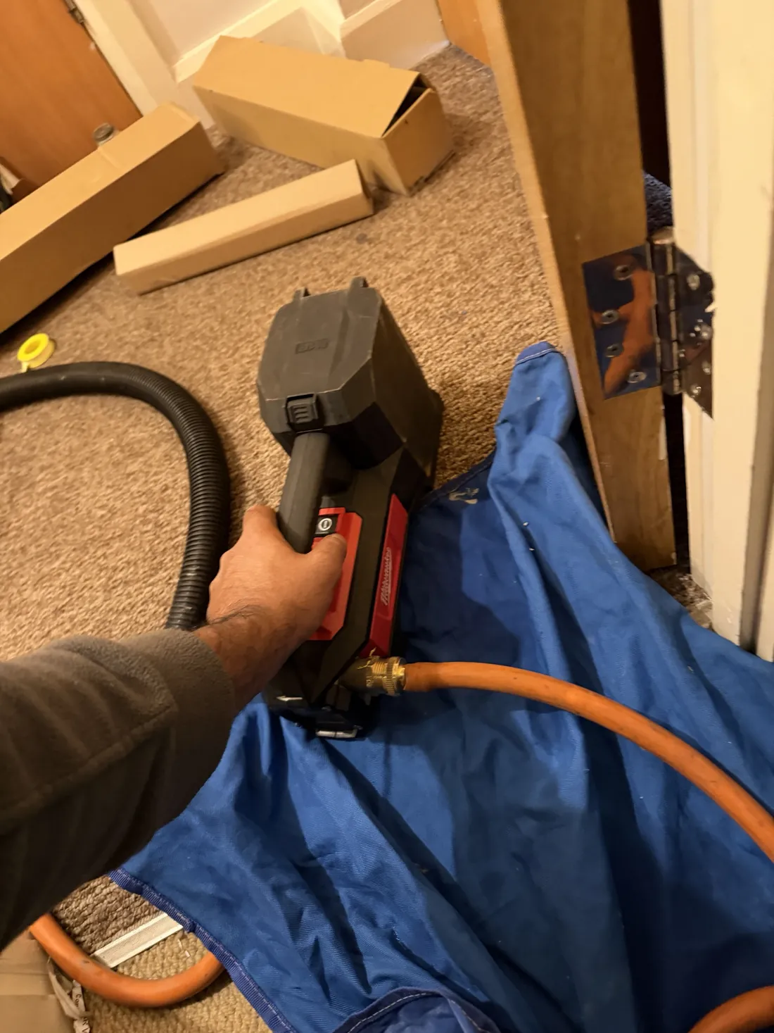 Engineer using a battery pump with an orange hose to drain down an unvented cylinder before replacing the immersion elements