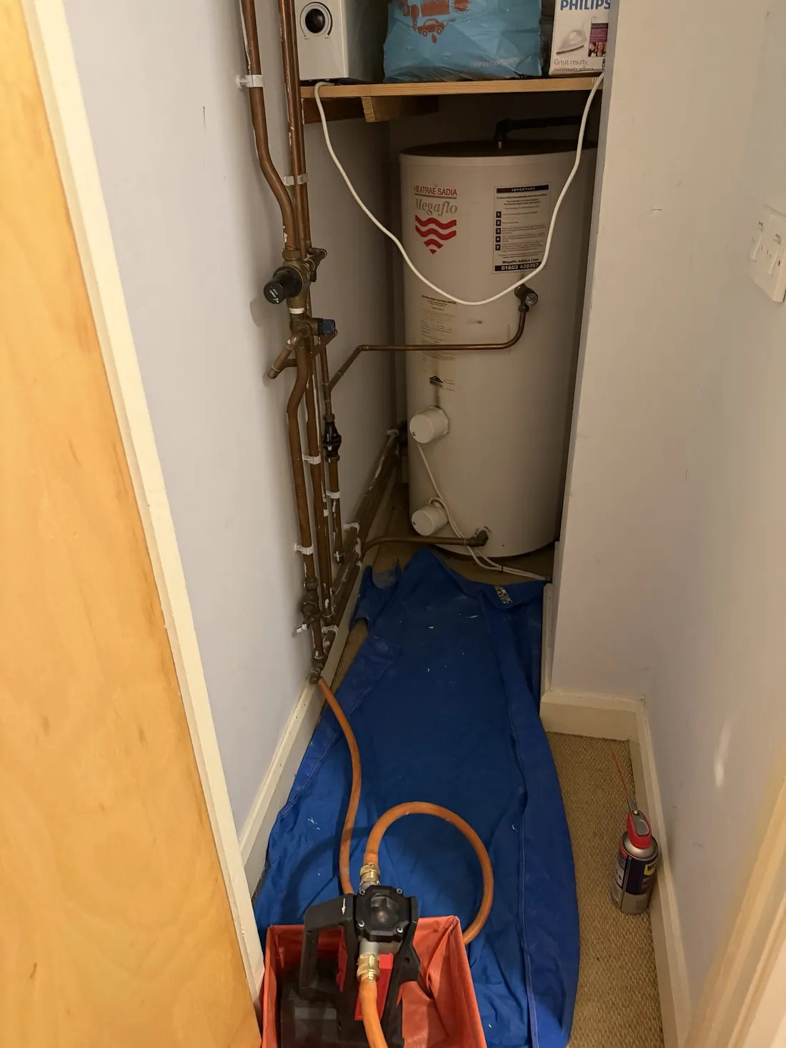 Cylinder cupboard with dust sheets down and an orange hose running from the drain-off point to a battery pump in a tray