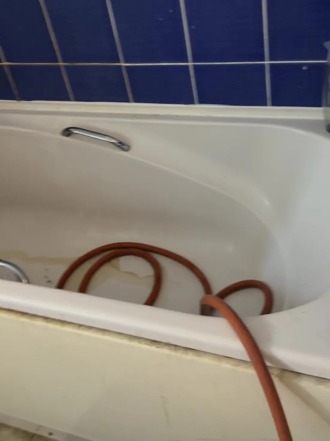 Orange drain hose laid in a bath, carrying the water pumped out of the unvented cylinder