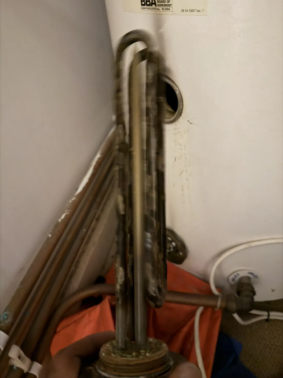 Old immersion heater element removed from a Megaflo cylinder, coated in scale and corrosion, with the empty boss in the cylinder behind