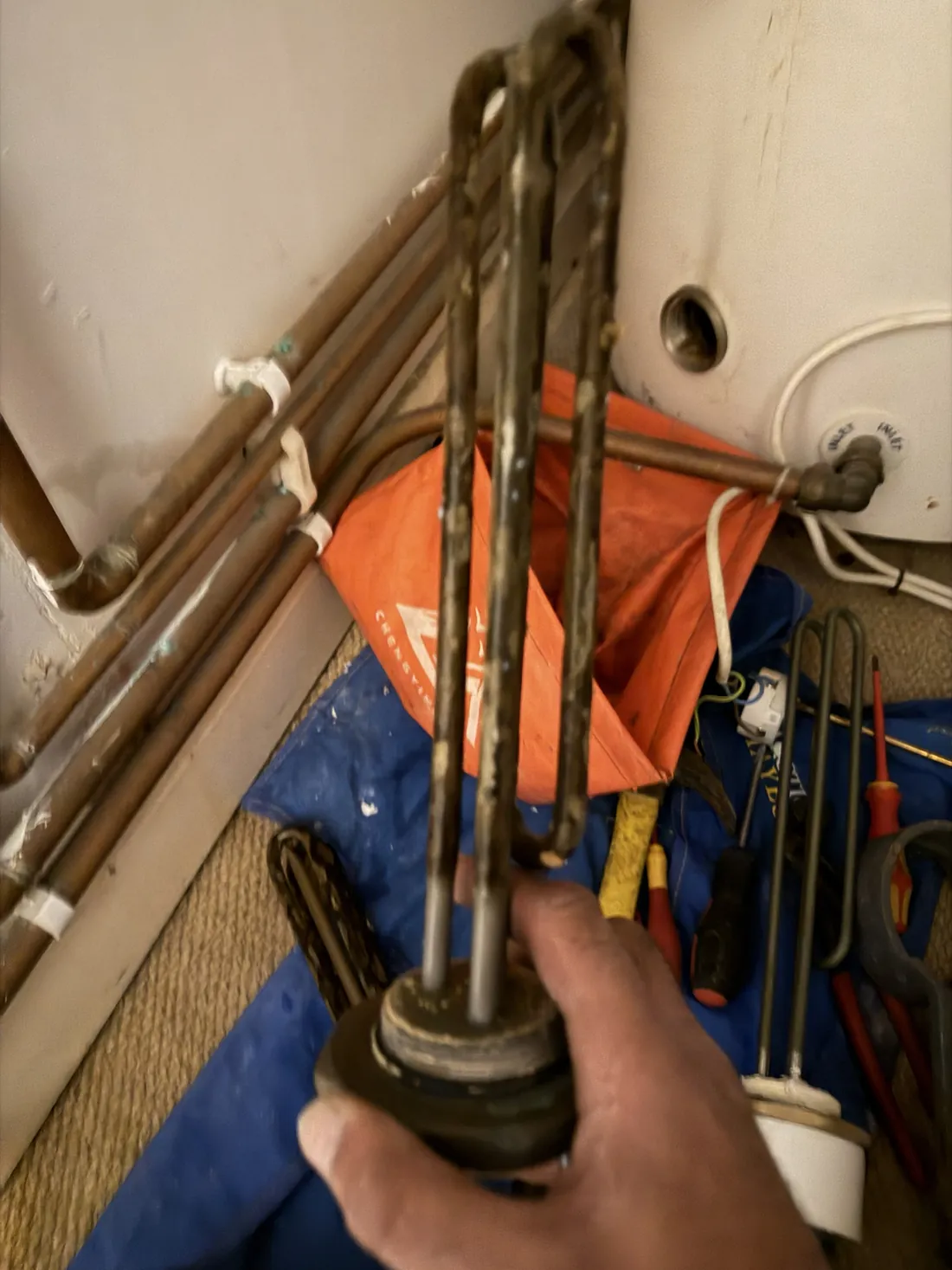A scaled old immersion element held in hand next to a second old element and a clean new replacement element on the floor
