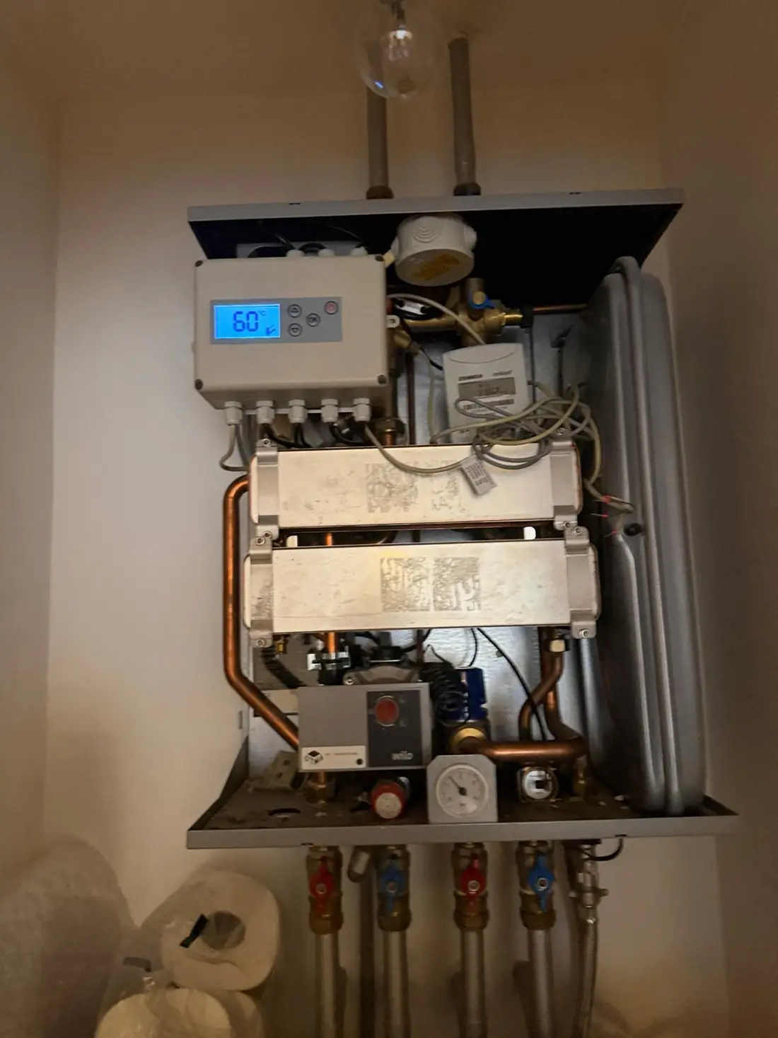 Heat interface unit in an apartment cupboard with the cover removed, showing the controller, plate heat exchangers and pump