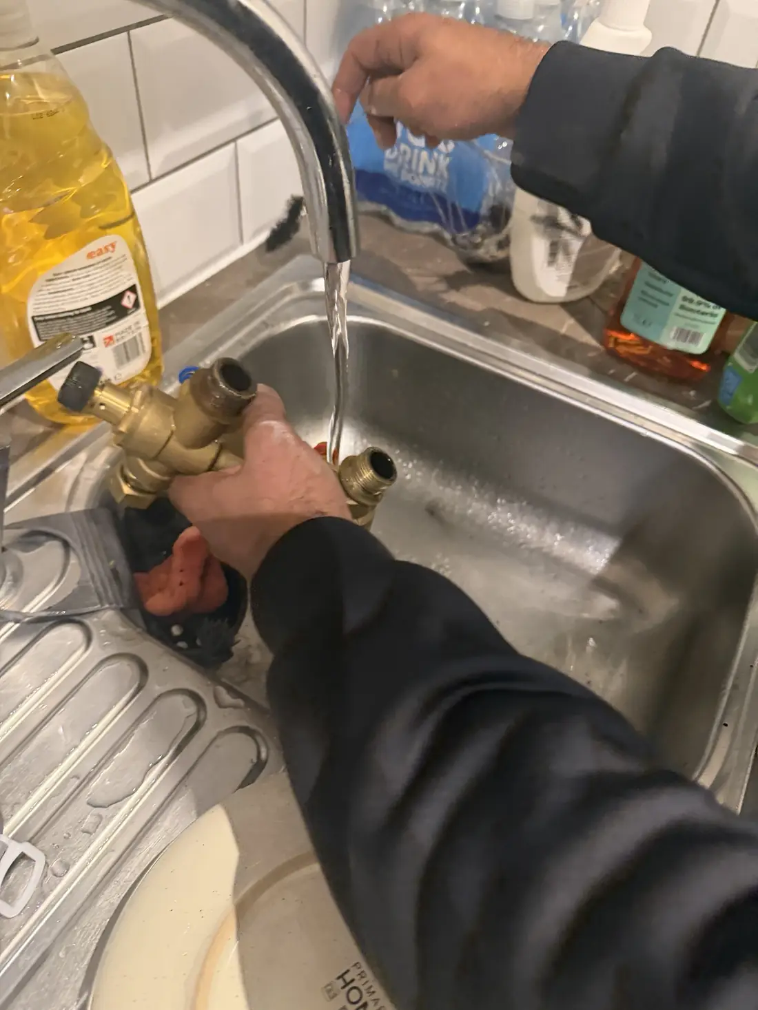Engineer holding the brass manifold and strainer assembly from the heat interface unit at a kitchen sink