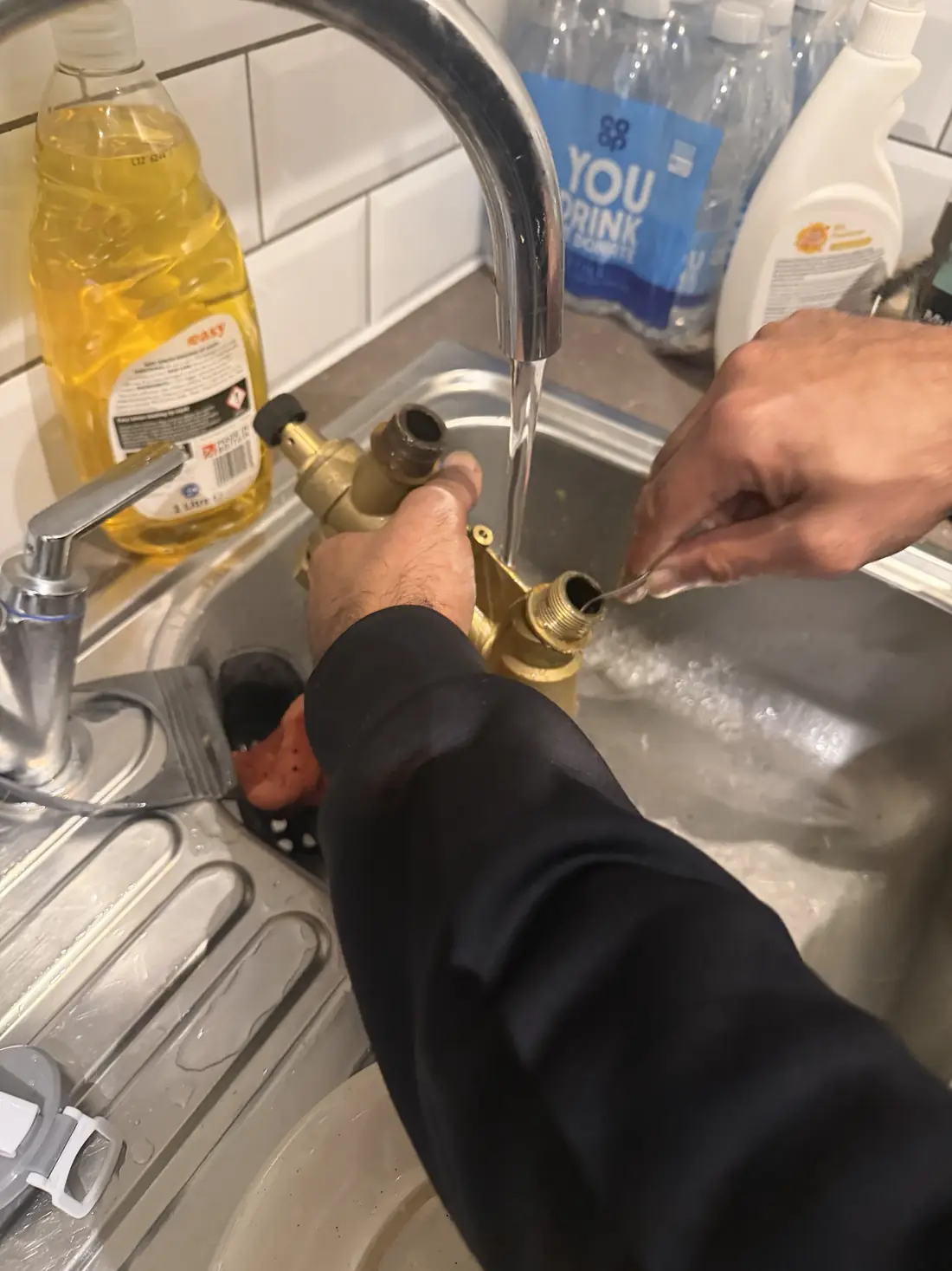 Engineer cleaning the seized strainer from the heat interface unit under a running kitchen tap