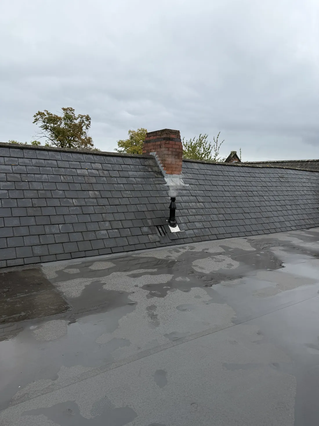 New black vertical boiler flue terminal coming through a slate roof next to a brick chimney