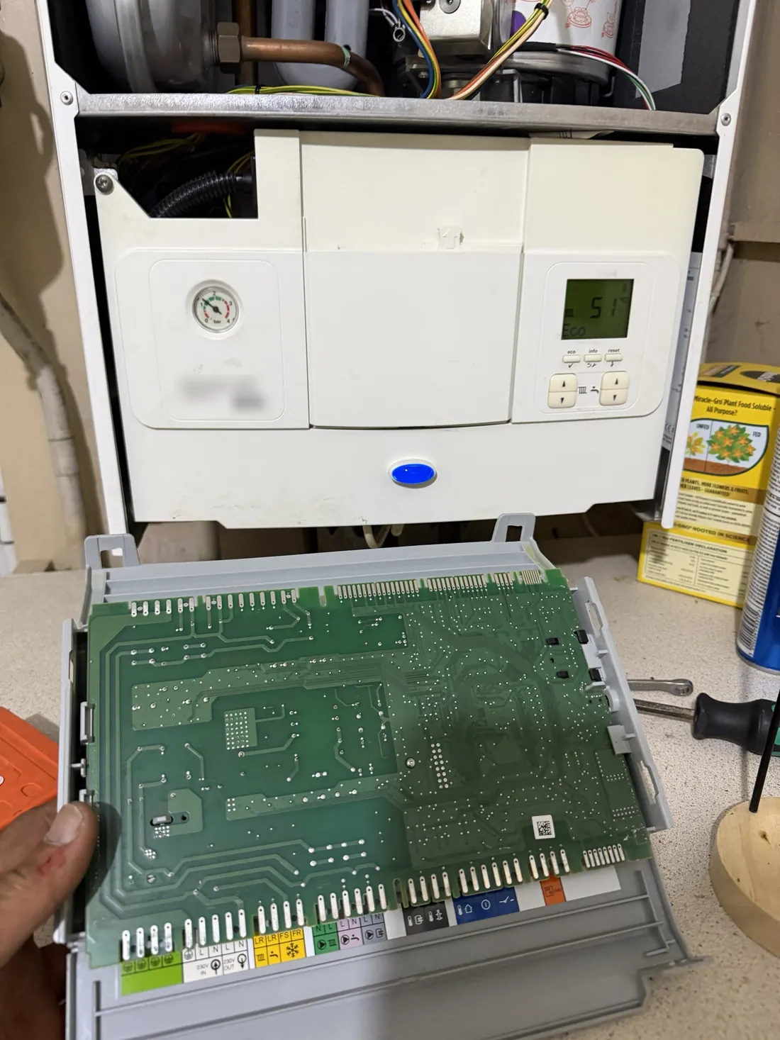 Faulty circuit board held out of a Worcester Greenstar 30i ErP, with the boiler running again behind it on a new board