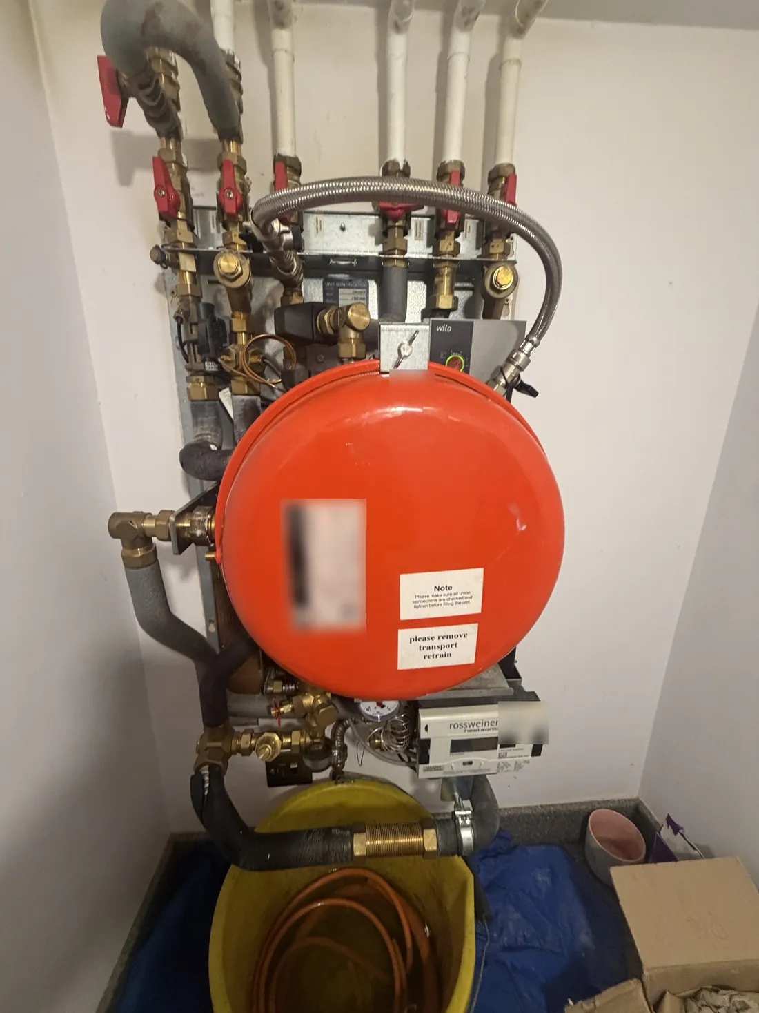 Meibes heat interface unit in a cupboard in a Newtown apartment, with its red expansion vessel, heat meter and isolation valves, dust sheets and a bucket below