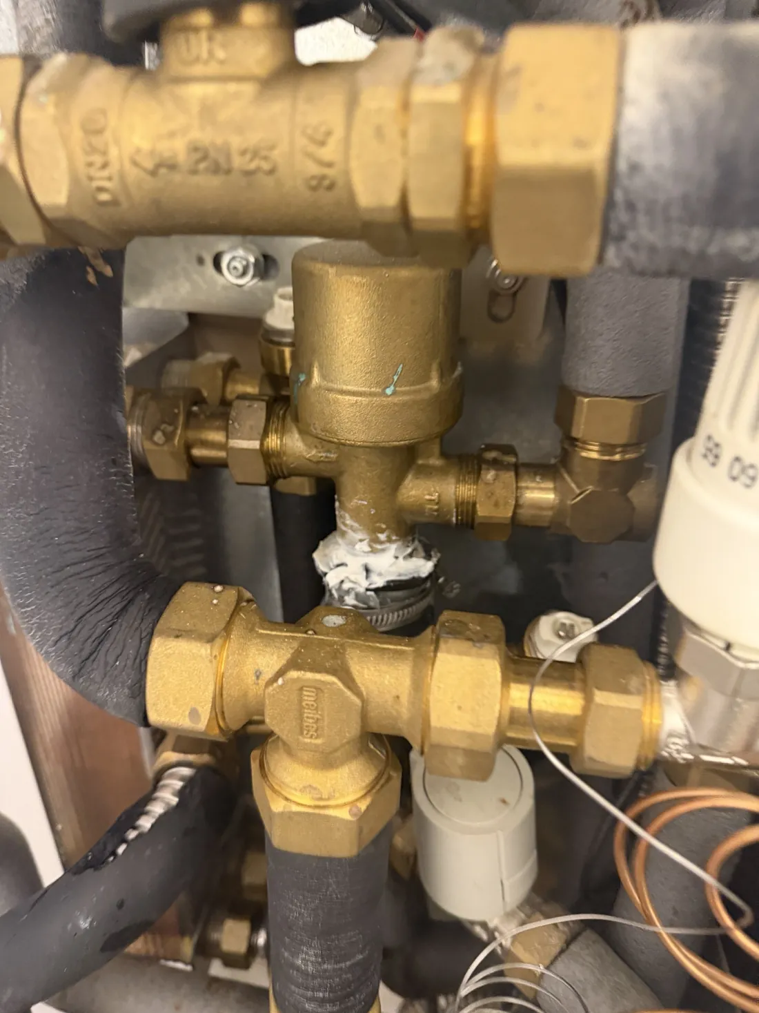 Brass PM valve inside a heat interface unit with a joint wrapped in white sealant and a hose clip