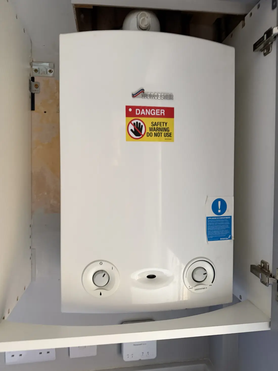 Old Worcester Greenstar Ri boiler in a kitchen cupboard with a Danger Do Not Use safety label on the case