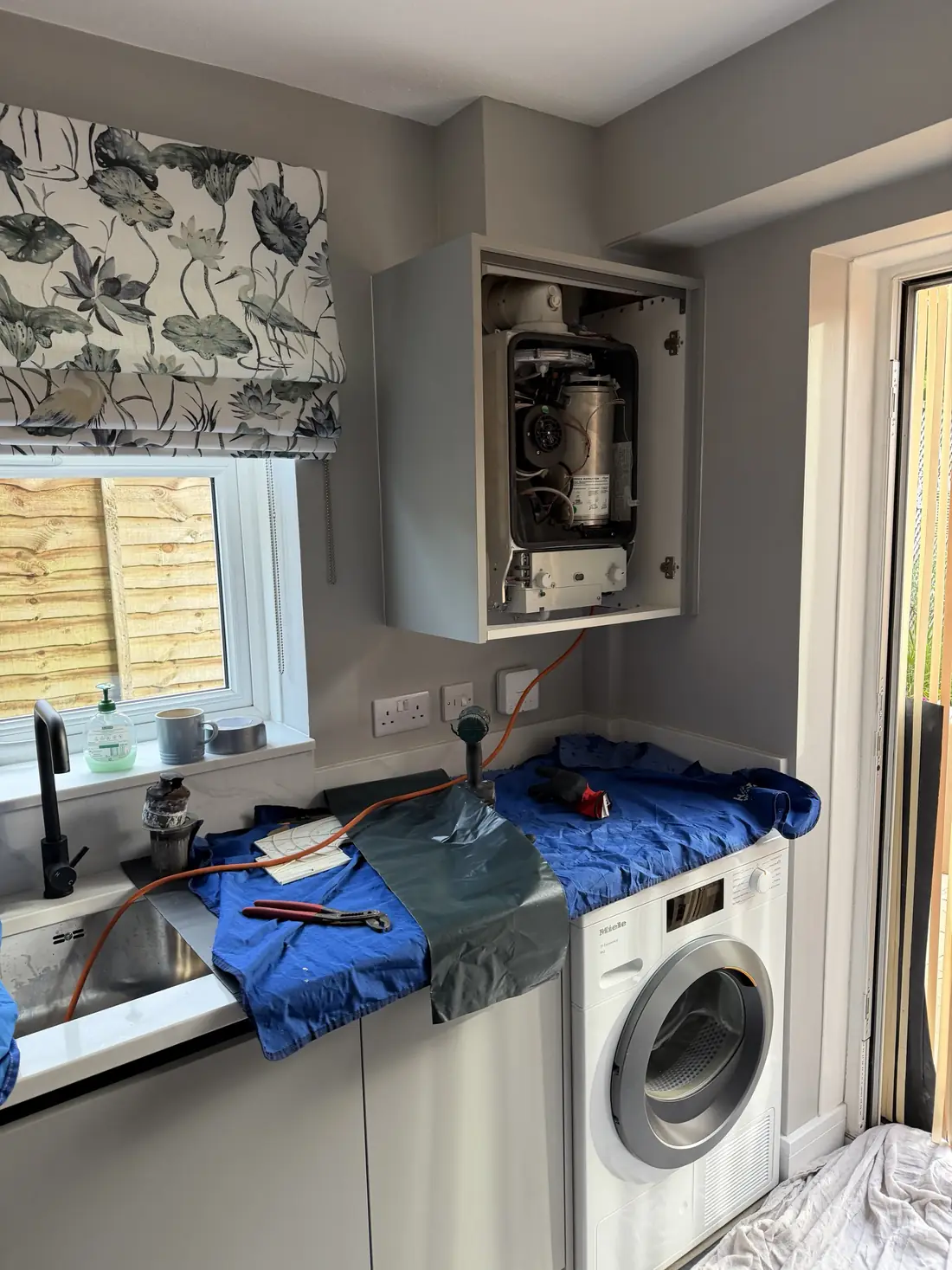 Kitchen with the boiler cupboard open and the old Worcester boiler partly dismantled, worktops covered with dust sheets