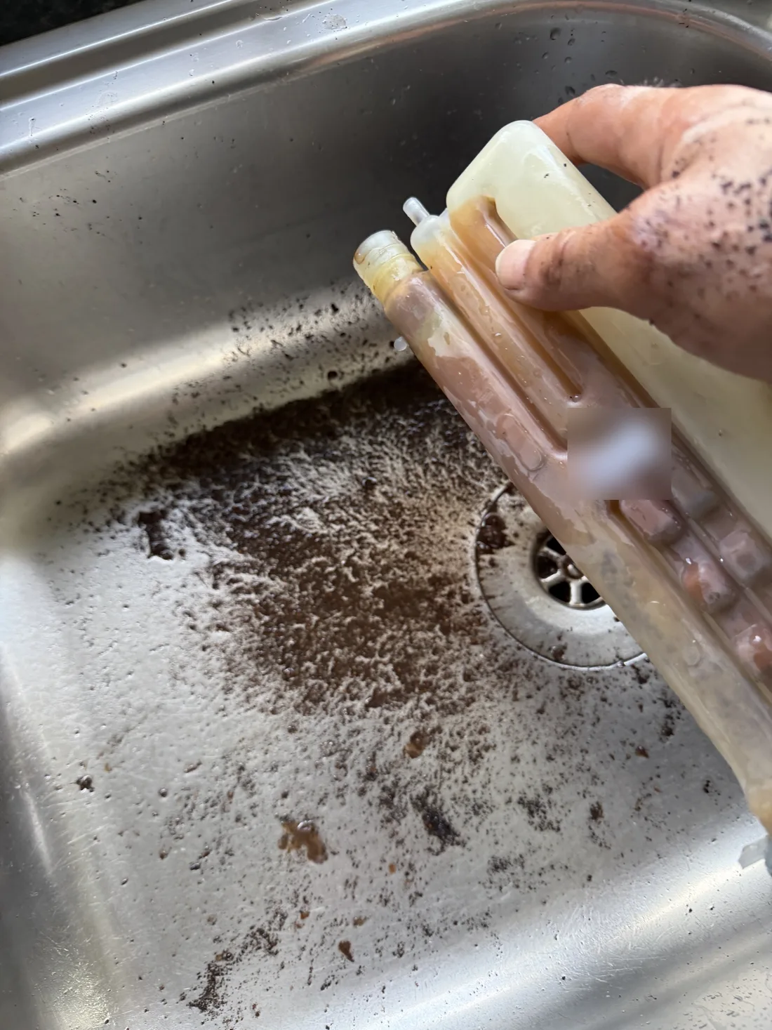 Condensate trap taken out of a Potterton boiler, stained brown, with the sludge and black debris that blocked it washed out into a sink