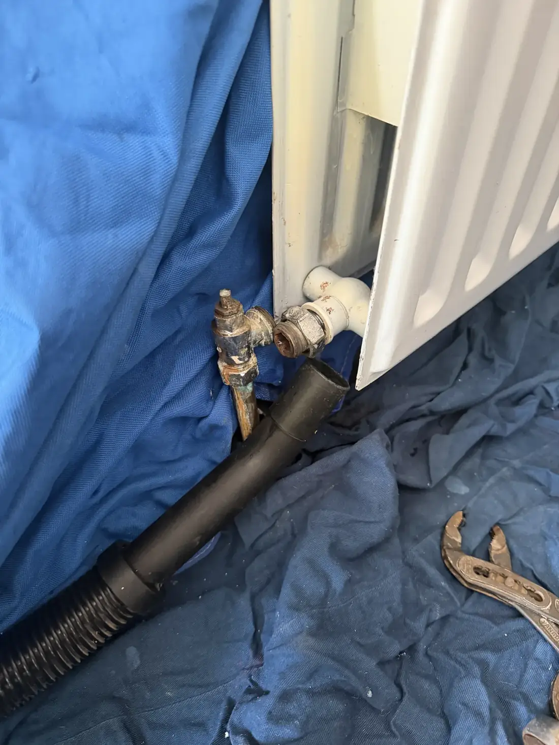 Radiator being drained through a hose with dust sheets protecting the floor, old valve removed