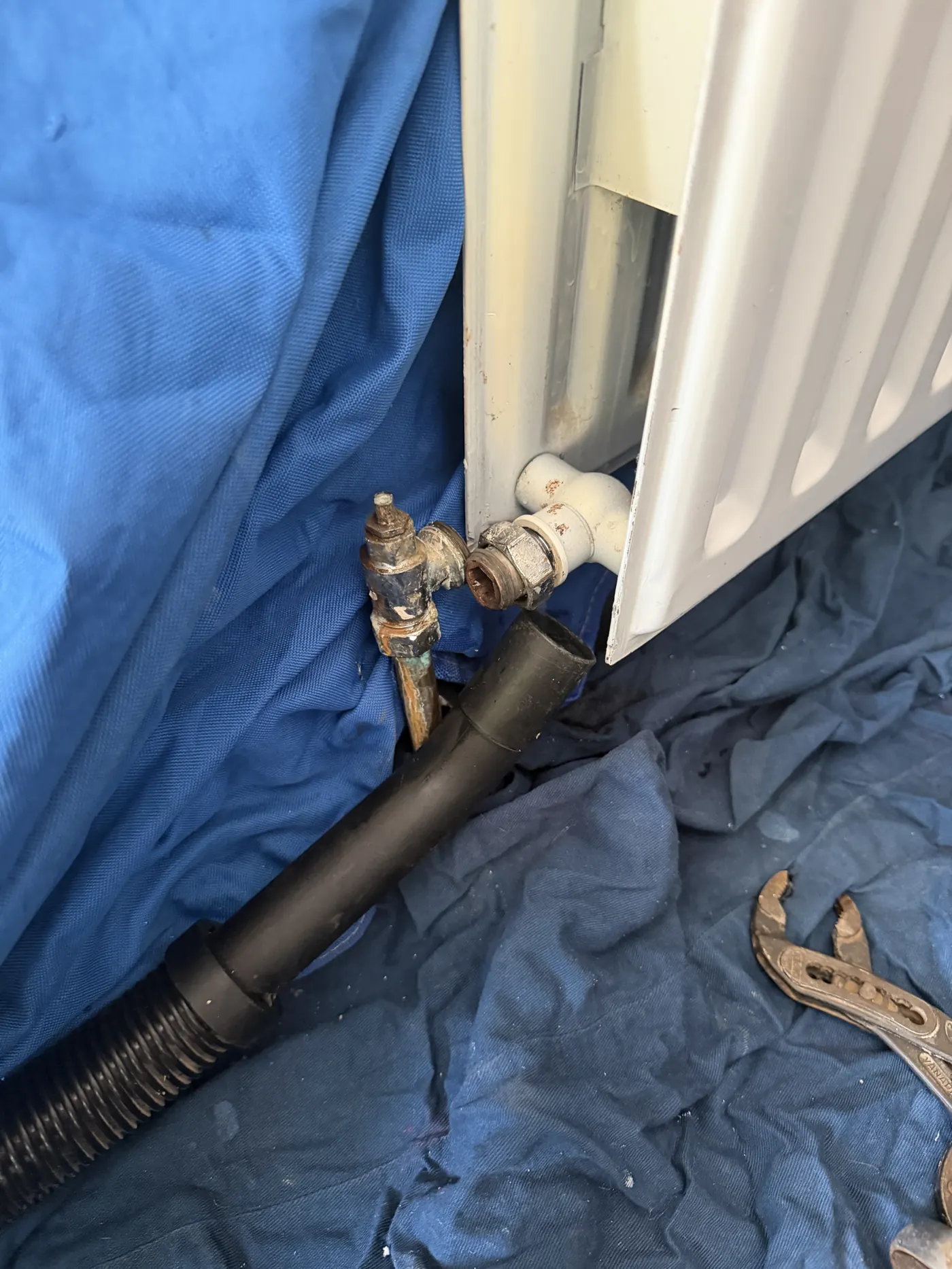 Radiator being drained through a hose with dust sheets protecting the floor, old valve removed