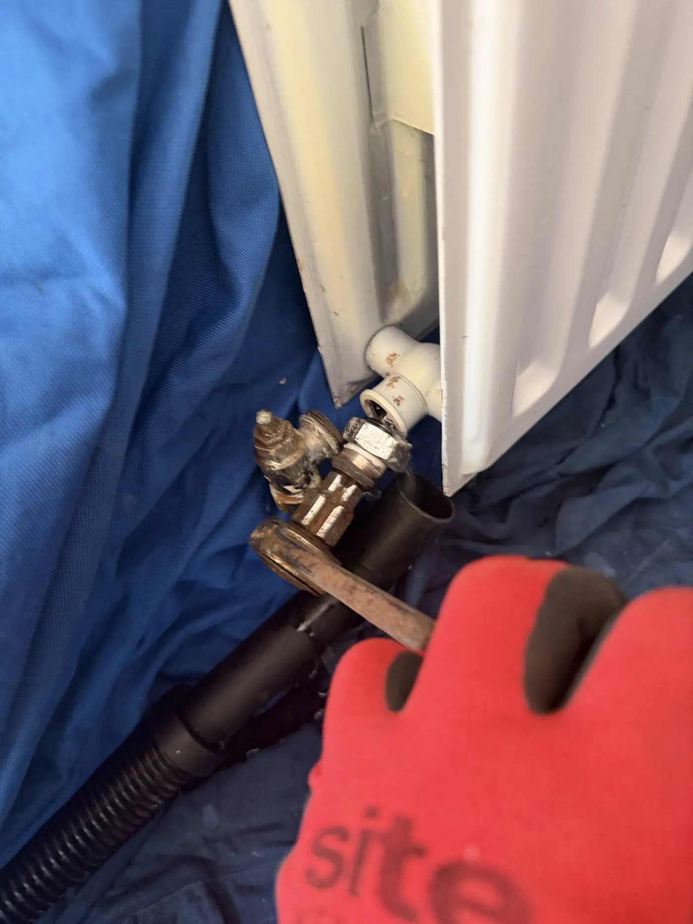 Engineer fitting a new radiator valve tail with a spanner, dust sheets underneath