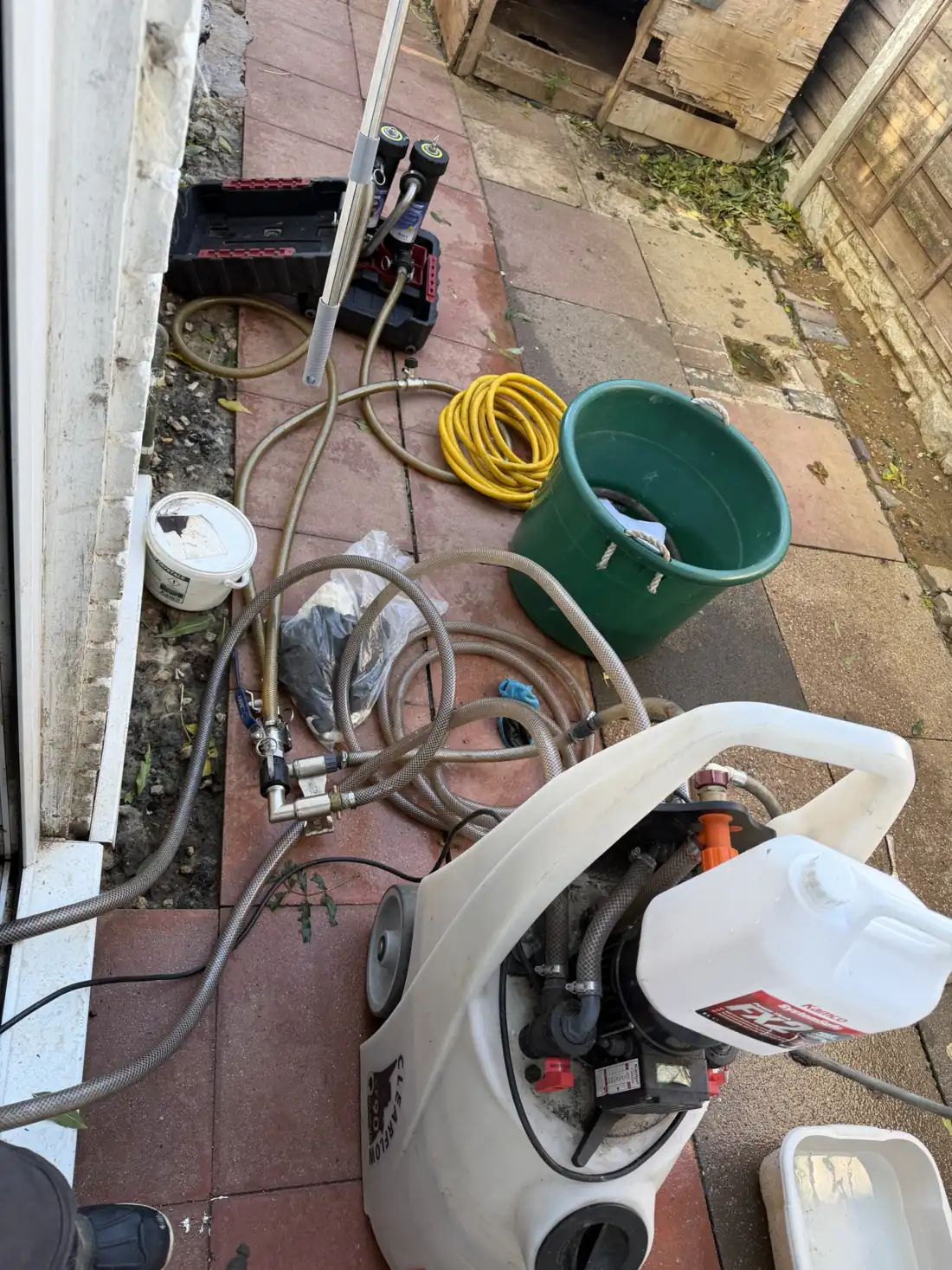 Power flushing machine set up outside a Wolverhampton rental, with hoses running to the heating system, a dump bucket and a bottle of system cleaner